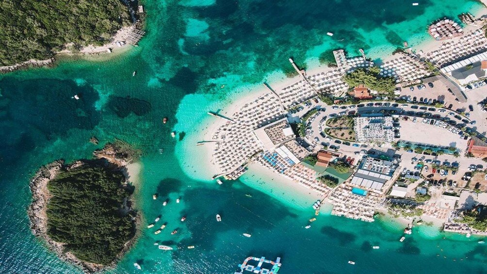 Vista aerea di una località balneare con acque turchesi cristalline, una spiaggia sabbiosa e numerose imbarcazioni. 5