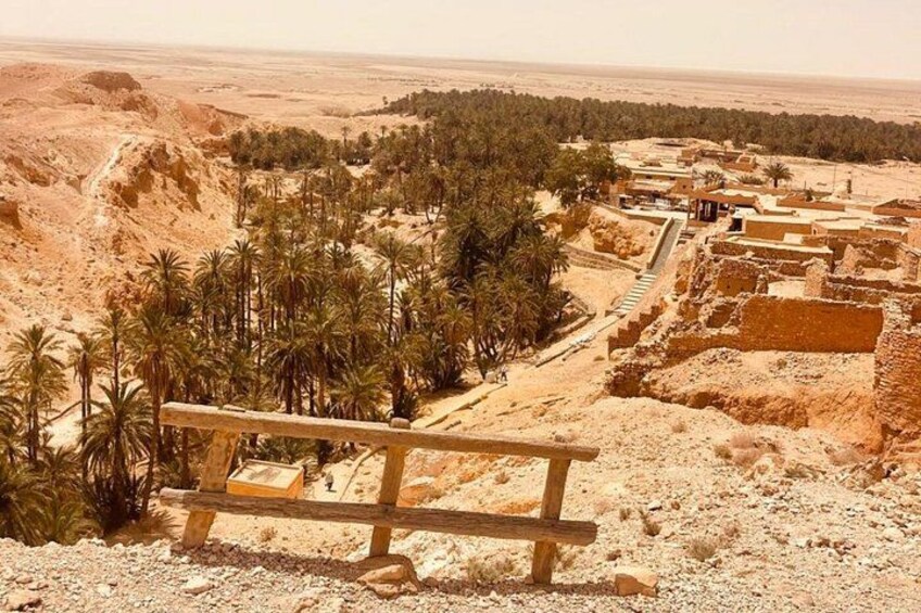 A desert landscape with ancient ruins, palm trees, and a wooden bench. 5