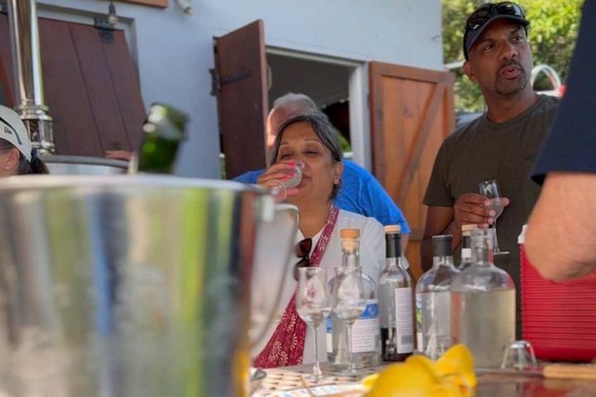 Un grupo de personas en un evento al aire libre, con una mesa llena de botellas y un gran contenedor metálico. 2