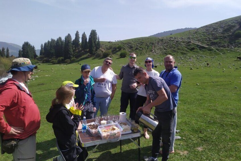 Un groupe de personnes s’est réuni autour d’une table où étaient disposés de la nourriture et des boissons, dans un cadre extérieur verdoyant. 2