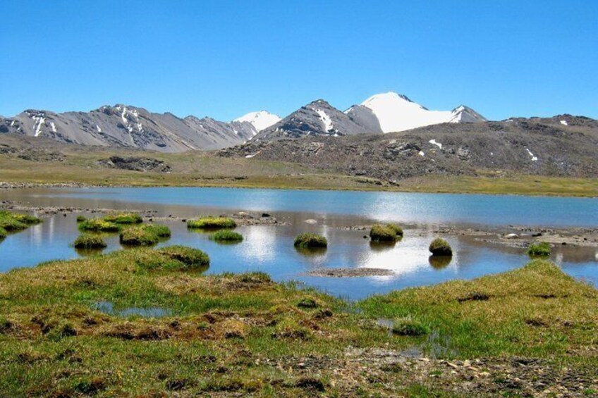 Un lac parsemé de taches de mousse verdoyante, entouré de montagnes dont les sommets sont couverts de neige. 5