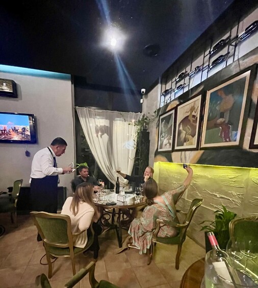 A restaurant interior with diners, a waiter, and a TV screen. 2
