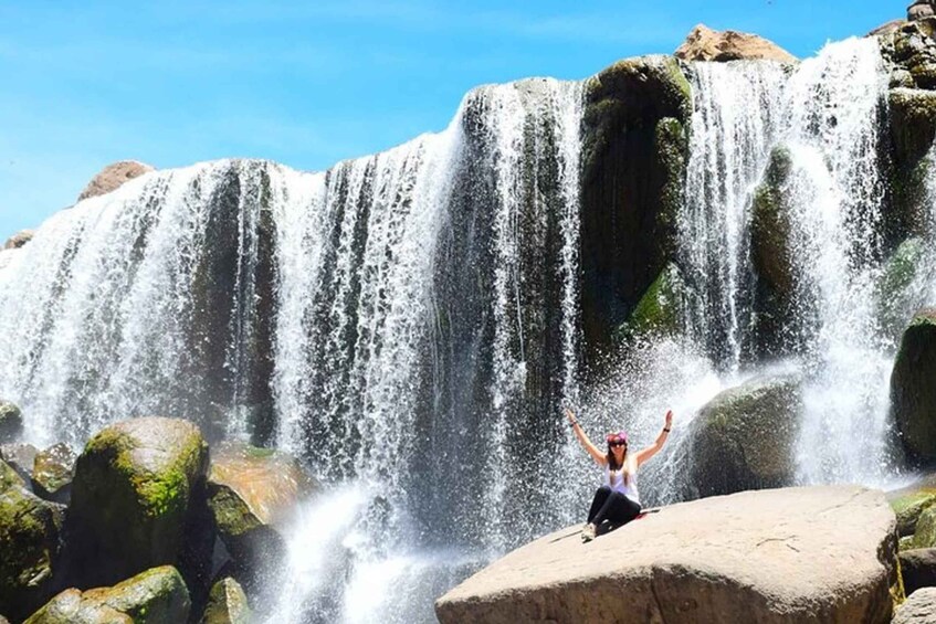 A person standing on a rock with arms raised in front of a waterfall. 2