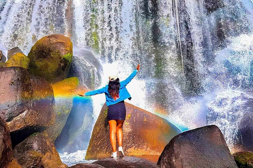 A person standing on rocks with arms outstretched in front of a waterfall. 4