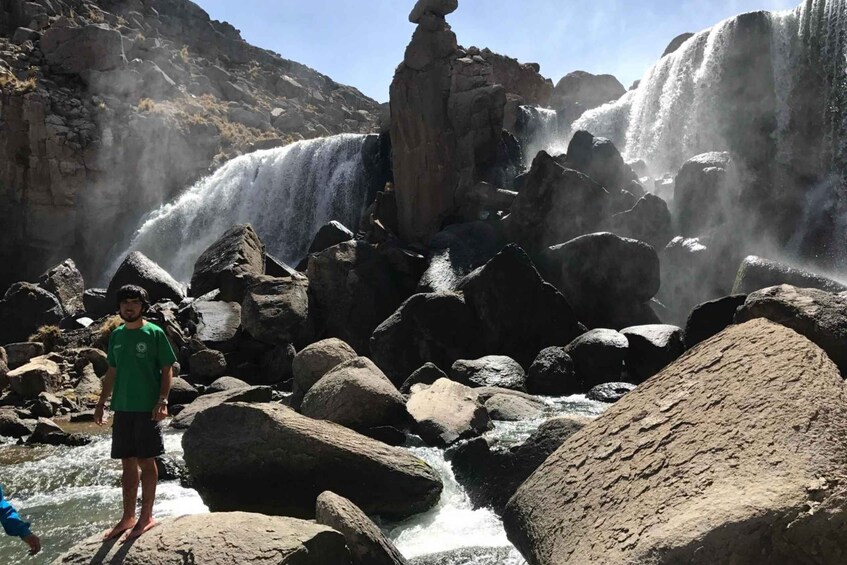 A waterfall cascading over rocks with a person standing in the foreground. 5