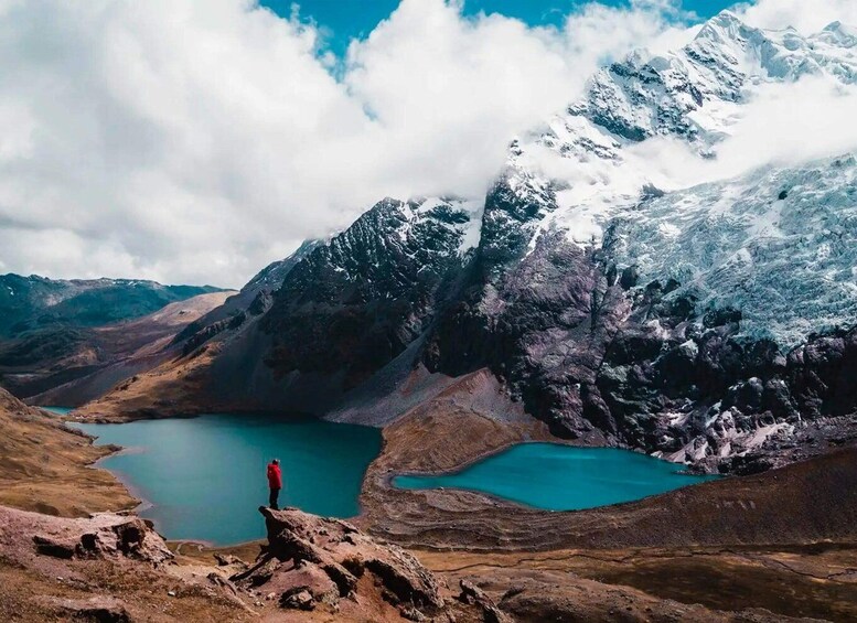 Une personne se tient debout sur un promontoire rocheux, surplombant un lac turquoise entouré de montagnes escarpées. 4
