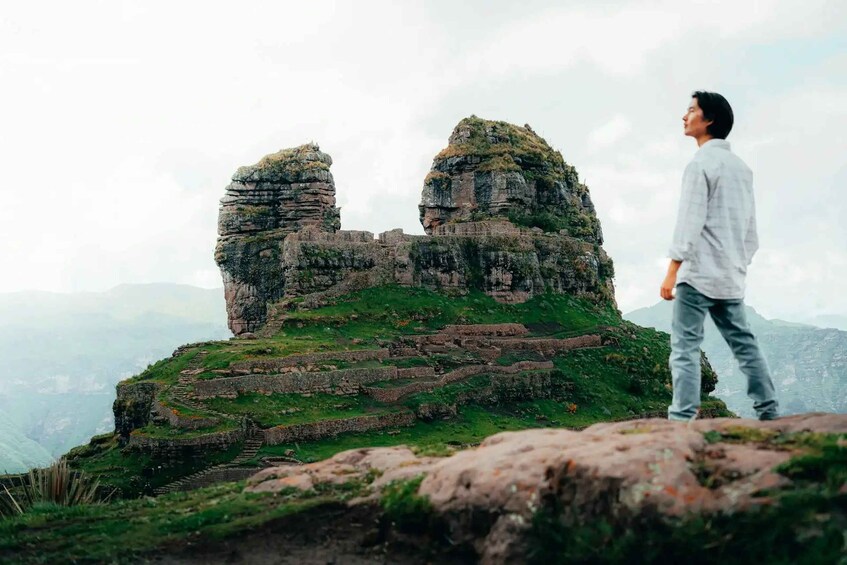 Une personne se tient debout sur un promontoire rocheux, avec des ruines anciennes et une végétation luxuriante en arrière-plan. 5