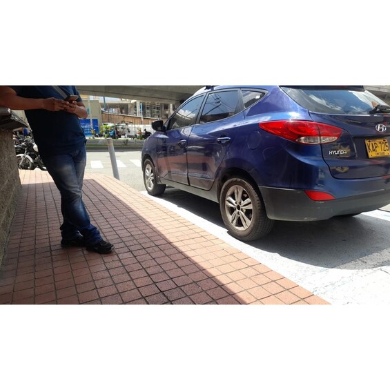 A blue Hyundai car parked on a brick sidewalk with a person standing nearby. 5