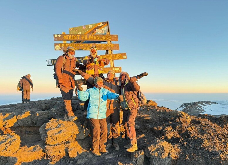A group of people celebrating at the base of Mount Kilimanjaro with a signpost. 4