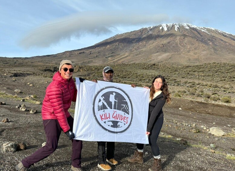 Three people holding a banner with a mountain in the background. 3