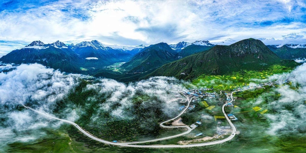 A mountainous landscape with a winding road, green fields, and snow-capped peaks. 3