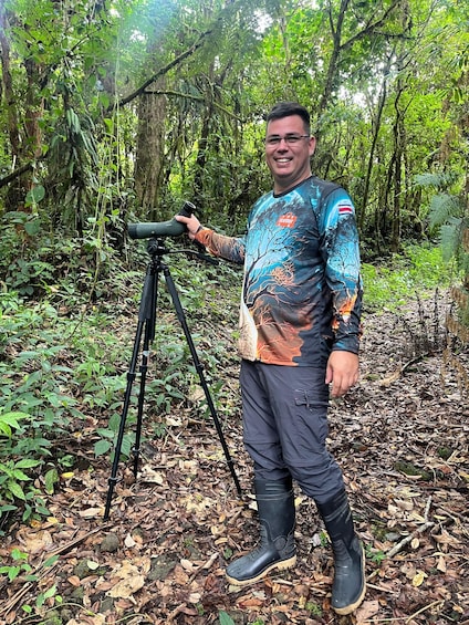 A person standing next to a camera on a tripod in a forest. 1