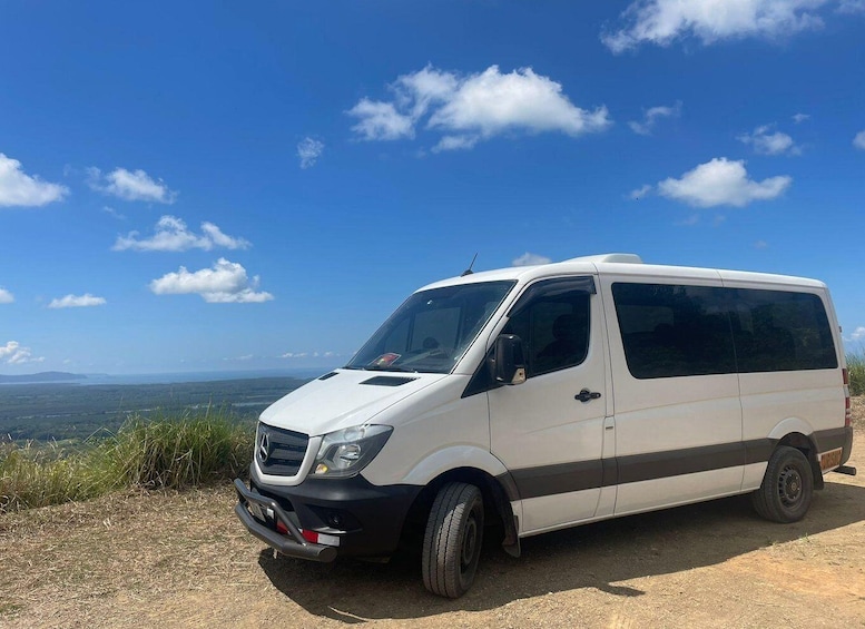 A white van parked on a dirt road with a scenic view of mountains and a clear blue sky. 2