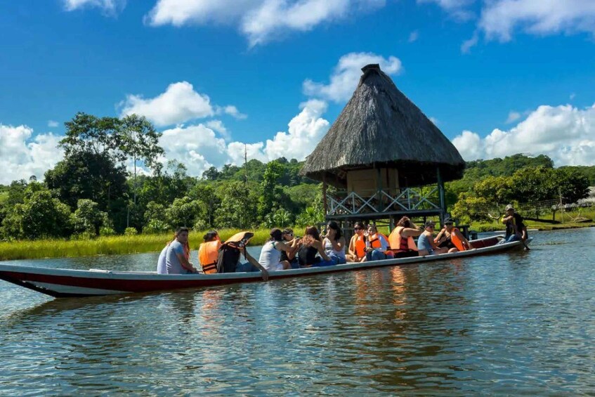 A group of people in a boat on a river, with a thatched-roof structure on the shore. 3