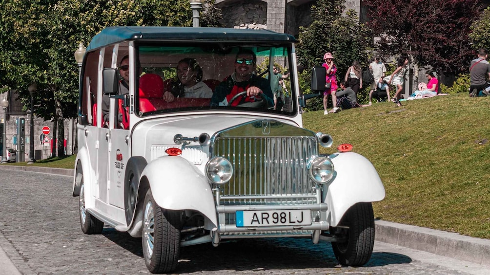 A vintage white car with a green roof driving down a cobblestone street. 1