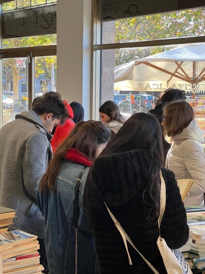 People browsing books at a bookstore with large windows and an umbrella outside. 2