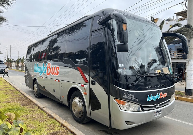 A black and silver Wayki Bus parked on a street with palm trees and buildings in the background. 1