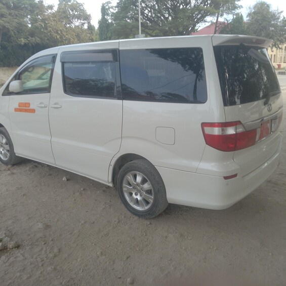 A white van parked on a dirt road with trees in the background. 4