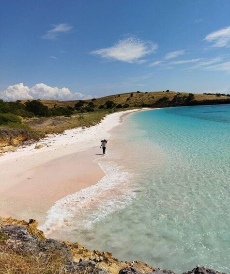 A beach with clear turquoise water, a person walking along the shore, and a hilly landscape in the background. 4