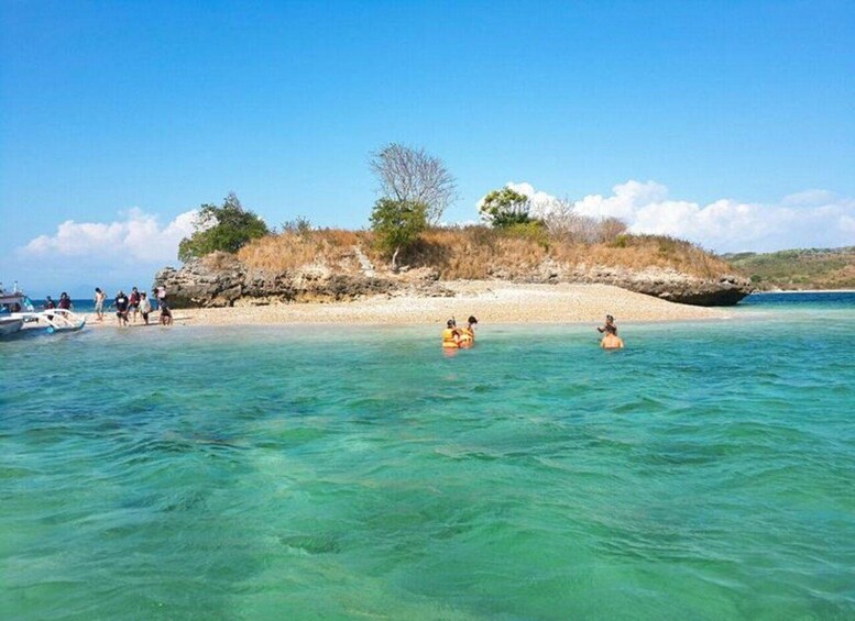 A beach with clear turquoise water, people in the water, and a boat in the background. 5