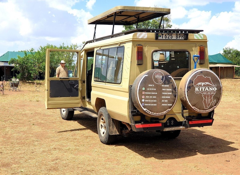 A beige safari vehicle with a roof, a man in a hat, and a sign advertising 'Kitano Tours and Safaris'. 1