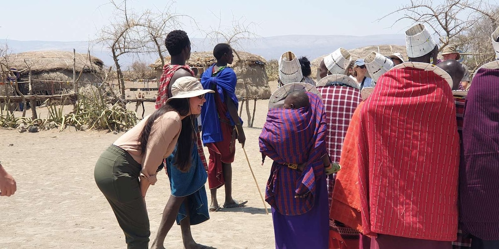 A group of people in traditional attire gathered outdoors, with thatched-roof huts in the background. 2