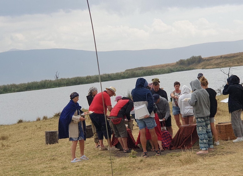 A group of people by a lake, some eating and others taking photos. 5