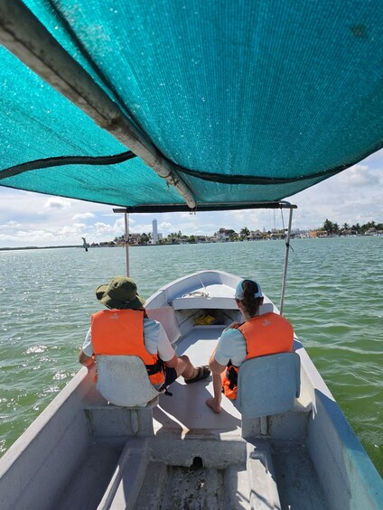 Two people in a small boat wearing life jackets, with a city skyline in the background. 2