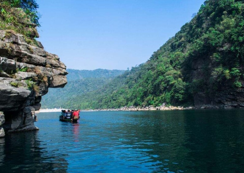 A boat with people on a calm river surrounded by rocky cliffs and dense greenery. 3