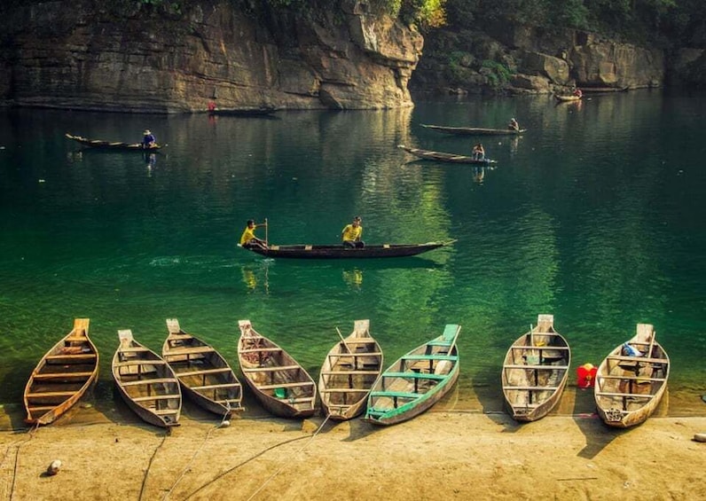 Several wooden boats on a calm river, with people paddling and standing in them. 2