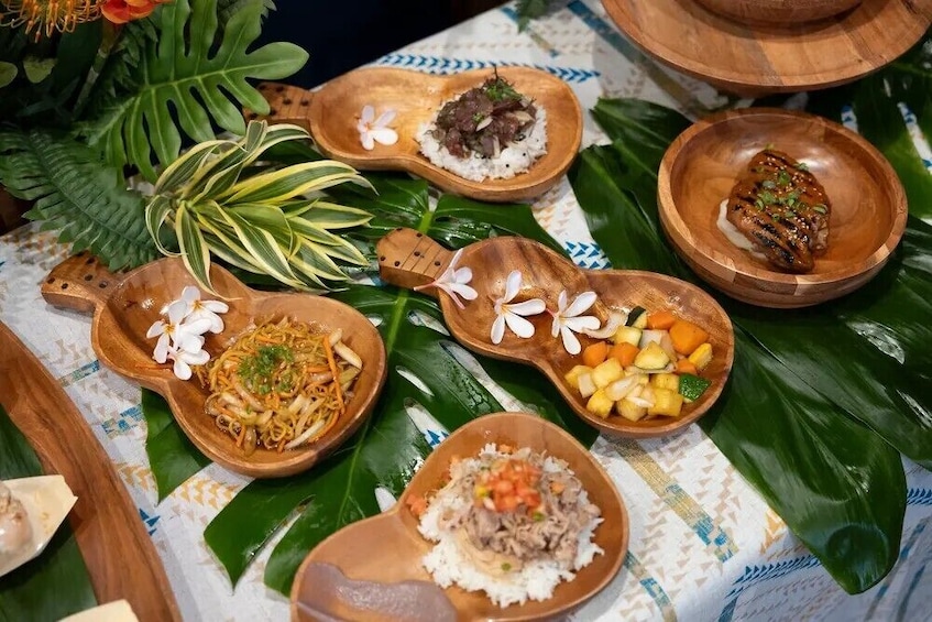 A variety of dishes served on wooden bowls with floral decorations, arranged on a table with green leaves. 5