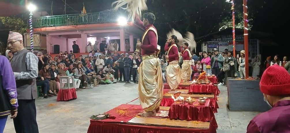 A cultural event with performers in traditional attire on a stage, an audience seated in the background, and a decorated outdoor setting. 3