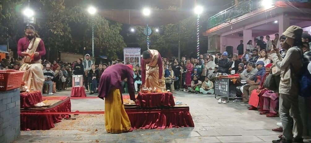 A public gathering with people seated on red mats, a stage with a speaker, and a crowd watching. 4