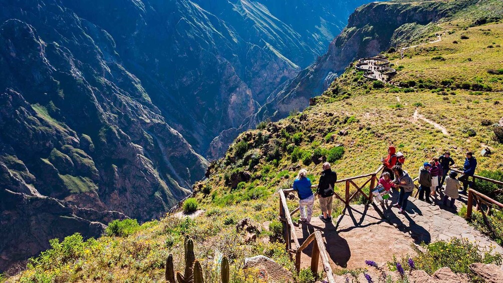 A mountainous landscape with a wooden viewing platform and people observing the scenery. 1