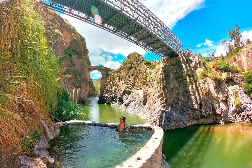 A person swimming in a natural pool under a bridge. 2