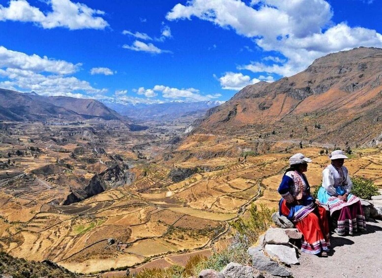 A mountainous landscape with terraced fields and two people sitting on a rock. 5