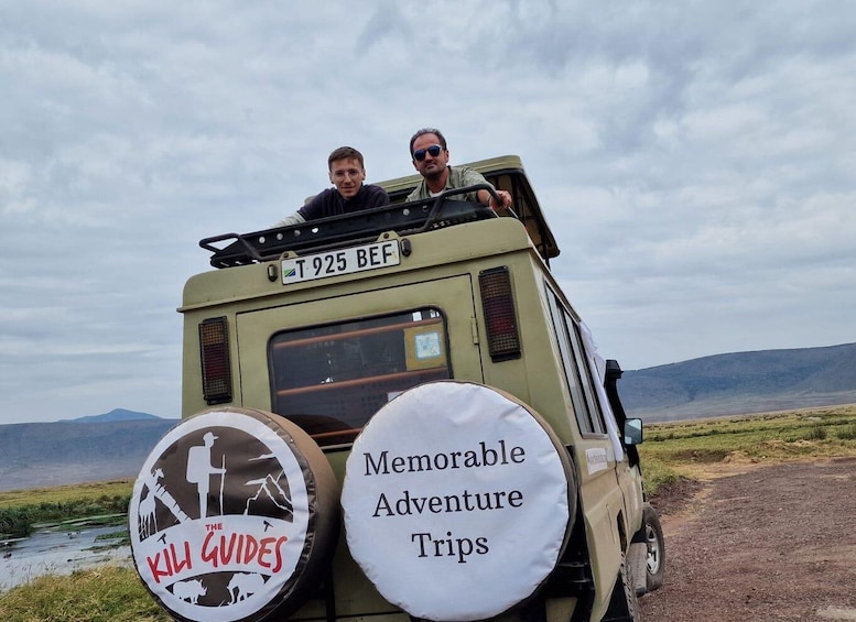 A safari vehicle with two passengers, a license plate reading "T 925 BEF", and two bumper stickers advertising "The Kill Guides" and "Memorable Adventure Trips". 1