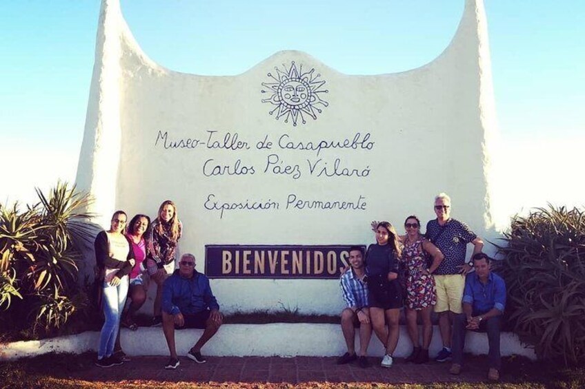A group of people posing in front of a sign for Museo-Taller de Casapueblo. 1