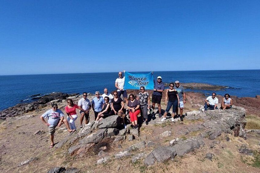 A group of people on a rocky coastal area with a clear blue sky and ocean in the background. 3