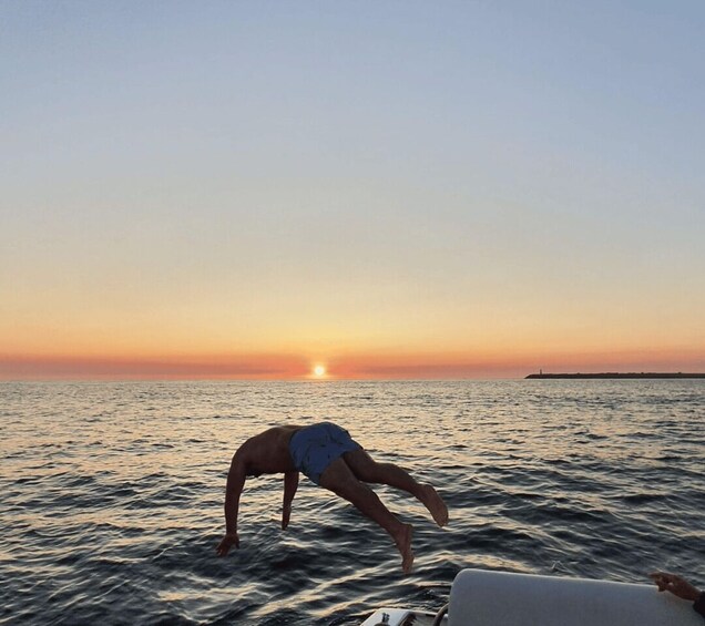 A person bending over in the water at sunset. 2