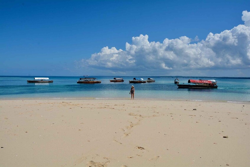 Una playa con una persona caminando, embarcaciones en el agua y un cielo despejado. 5