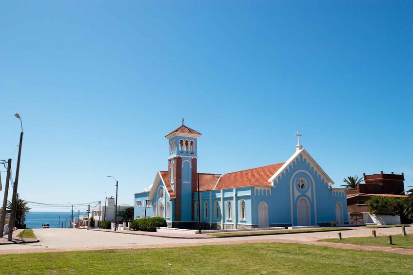 A blue church with a bell tower and a red roof, surrounded by a green lawn and a clear blue sky. 4
