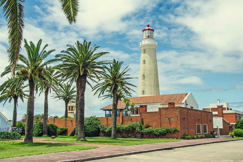 A lighthouse with a red top, surrounded by palm trees and a brick building. 3