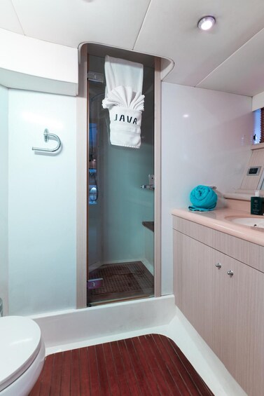 A bathroom with a glass shower enclosure, a white towel hanging on the door, and a blue towel on the counter. 4