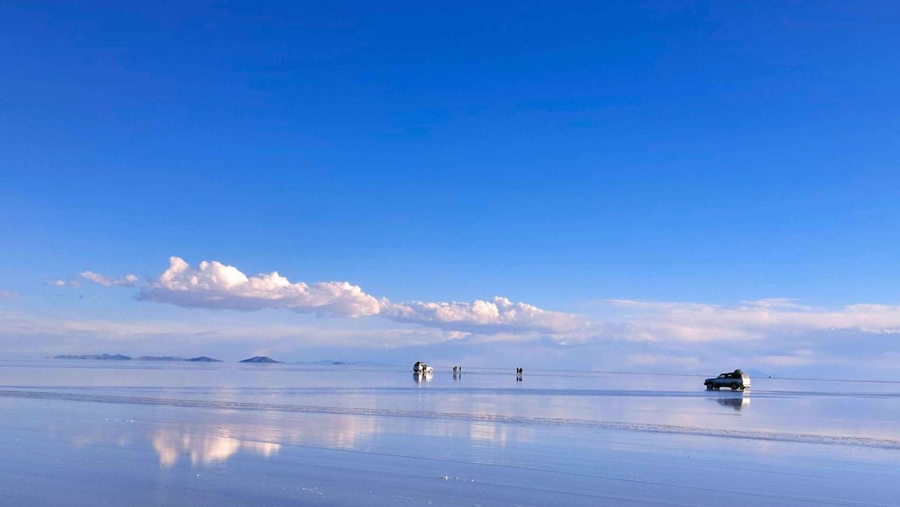 A vast salt flat with a clear blue sky, a few people, and a vehicle. 4