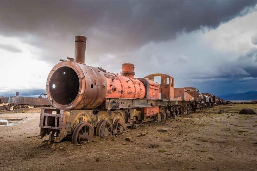 An abandoned, rusted train engine with a large cylindrical tank, set against a cloudy sky. 2