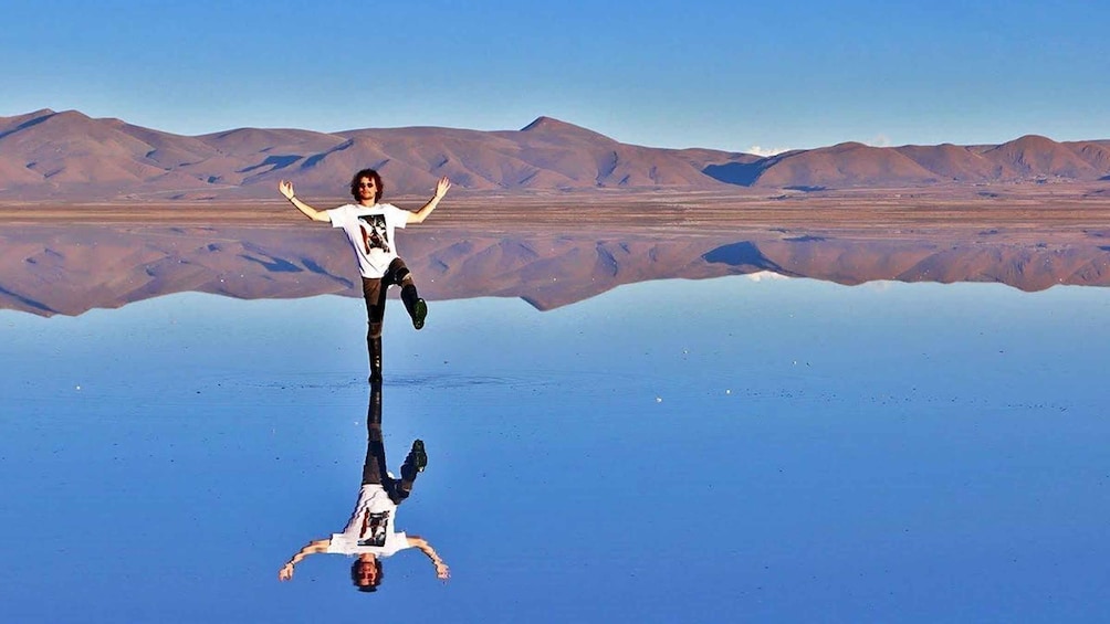 A person standing on a reflective surface with mountains in the background. 5