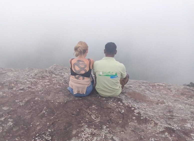 Two people sitting on a rocky outcrop overlooking a misty landscape. 1