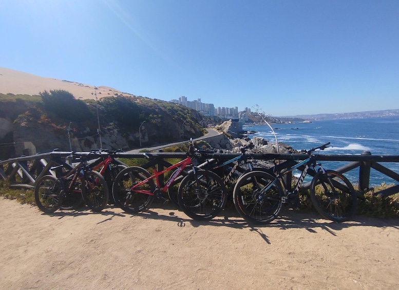 A coastal road with bicycles parked on a fence, overlooking the ocean and a city skyline. 1