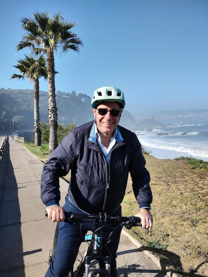 A person riding a bicycle on a coastal path with palm trees and ocean in the background. 5